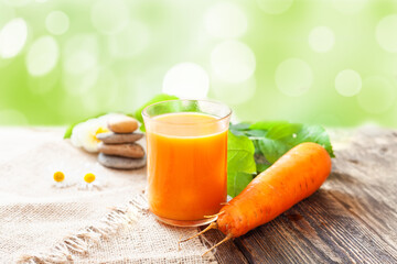 A glass of carrot juice and ripe carrots on the table