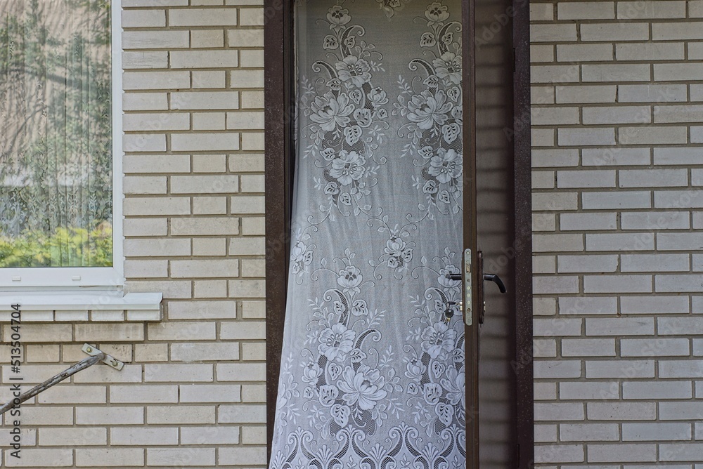 Poster one open brown metal door with a white curtain on a gray brick wall with a window on the street