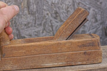 hand holding a brown old wooden planer over a plank on a gray background in a workshop