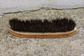 one old brown wooden clothing brush with black plastic bristles on a gray concrete table