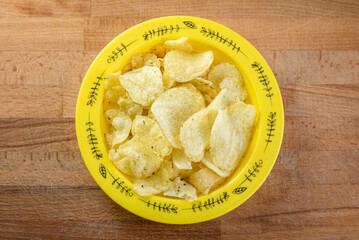Potato chips in a yellow bowl on a wooden table closeup shot