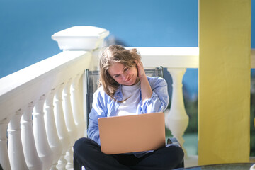 A happy freelance woman works on a balcony with a laptop on the background of the sea.