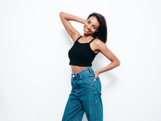 Portrait of young beautiful black woman. Smiling model dressed in summer jeans clothes. Sexy carefree female posing near white wall in studio. Tanned and cheerful