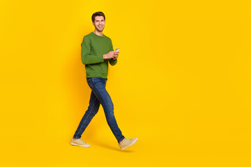 Fototapeta na wymiar Photo of charming pretty guy dressed green pullover writing modern device walking empty space isolated yellow color background