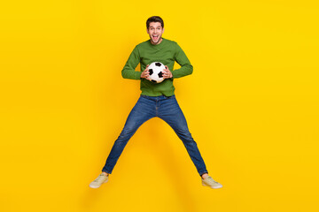 Fototapeta na wymiar Photo of cute impressed guy dressed green pullover jumping high holding ball isolated yellow color background