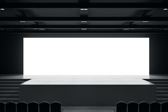 Front view on big blank white illuminated screen with space for your text or logo in empty huge hall with scene, stairs and rows of seats. 3D rendering, mockup