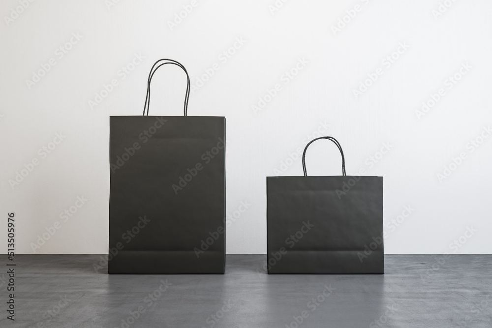 Poster front view on two black blank paper shopping bags with place for your logo or text on concrete floor