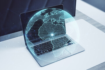 Close up of workplace with laptop and creative glowing polygonal grid planet on blurry background. Globe, international map, communication, network earth and technology concept. Double exposure.