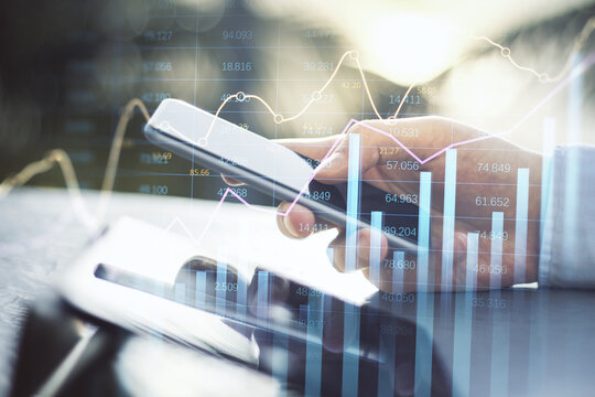 businessman hand using smartphone and tablet at desktop with abstract glowing business chart with index and growth on blurry background. Finance, trade and market report concept. Double exposure.
