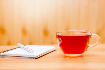 Cup of tea and notebook with pen on the table in the morning