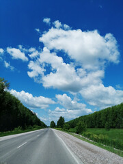 white clouds in the vast blue sky, road ahead with greenery on the sides, summer travel