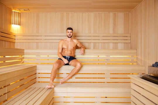 A muscular man in swimwear sitting in a sauna and relaxing after a busy week.