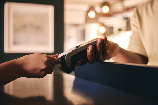 Close In Of Sales Assistant In Retail Shop With Customer Paying Using Contactless Payment Credit Card NFC