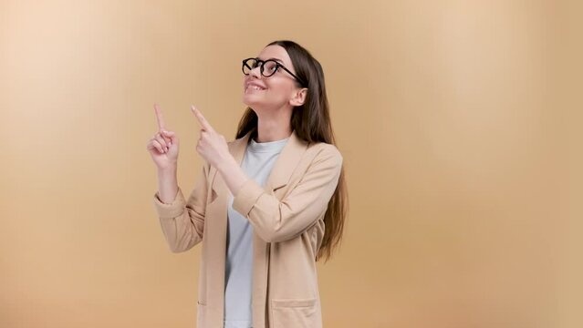 Cheerful smart looking casually dressed lady pointing aside over beige background.