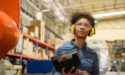 A young female worker is controlling a mechanical robot. to sort out the items that come into the...