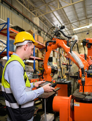 A male worker is controlling a welding robot. by using forcing welding with a control screen which...