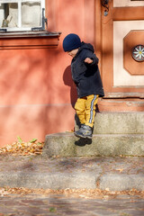 A cute boy in a autumn jacket with a blue hat goes for a walk around the old town. The child is self-climbing the stairs