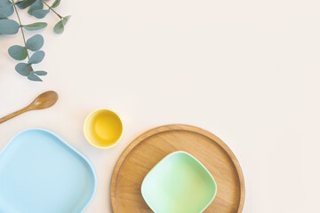 Baby accessories and tableware for food on beige background. First feeding for kids concept. Flat lay, Top View, Space for text. Silicone dishware, bib, cup on neutral backdrop. Serving baby food