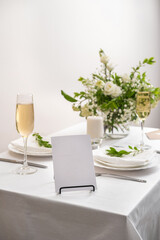 Mockup white blank space card for table number or menu. Wedding teble decoration with white flowers, glasses and white napkins. Elegantly decorated table at a wedding reception. 