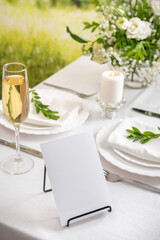 Mockup white blank space card for table number or menu. Wedding teble decoration with white flowers, glasses and white napkins. Elegantly decorated table at a wedding reception. 