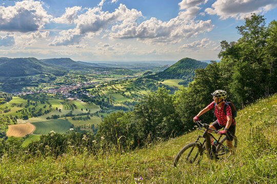 nice senior woman riding her electric mountainbike at a viewpoint on the Swabian Alb above village of Neidlingen, Baden-Württemberg, Germany
