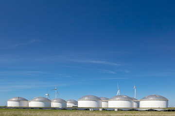 Large Dutch gas and fuel storage tanks with wind turbines and solar panels in front in the...