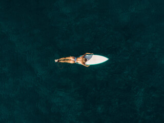 Obraz premium Pretty surfer woman floating on surfboard in ocean. Aerial view