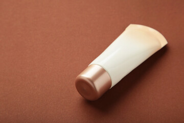 Tube of cream or gel white plastic product on brown background.