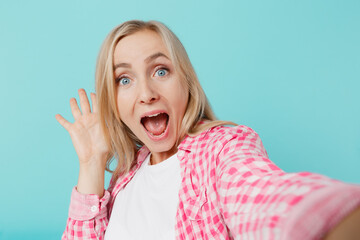 Close up young shocked woman she 30s in pink shirt white t-shirt doing selfie shot pov on mobile cell phone waving hand isolated on plain pastel light blue background studio People lifestyle concept