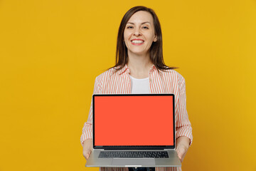 Young happy smiling secretary copywriter woman she 30s in striped shirt white t-shirt hold use work on laptop pc computer with blank screen workspace area isolated on plain yellow background studio