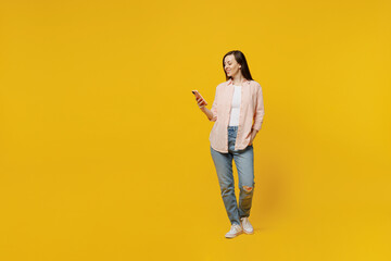 Full body young happy smiling cheerful woman she 30s wears striped shirt white t-shirt hold in hand use mobile cell phone isolated on plain yellow background studio portrait. People lifestyle concept.