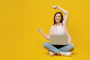 Full body young happy secretary copywriter woman she in striped shirt white t-shirt hold use work on laptop pc computer point index finger aside on workspace area isolated on plain yellow background.