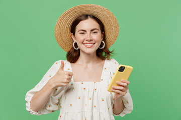 Young happy smiling satisfied fun woman she 20s wears white dress hat hold in hand use mobile cell phone show thumb up isolated on plain pastel light green background studio. People lifestyle concept.