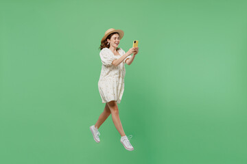 Full body side view young happy woman she 20s wears white dress hat hold in hand mobile cell phone jump high isolated on plain pastel light green background studio portrait. People lifestyle concept.