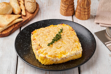 Potato gratin covered with cheese, cream and sprig of greenery  freshly served from the oven on a wooden table.