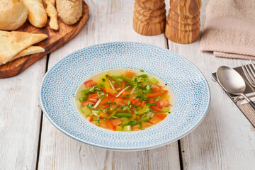 Vegetable soup in white bowl surrounded by ingredients on wooden table. Menu concept.  