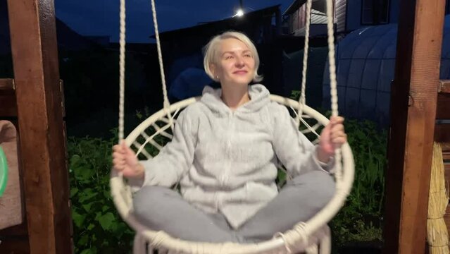 The girl swings on a swing in the evening and smiles