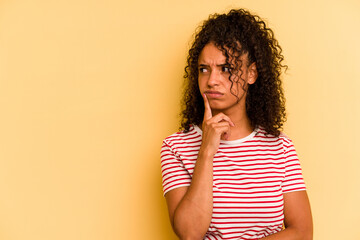 Young Brazilian woman isolated on yellow background looking sideways with doubtful and skeptical expression. - obrazy, fototapety, plakaty
