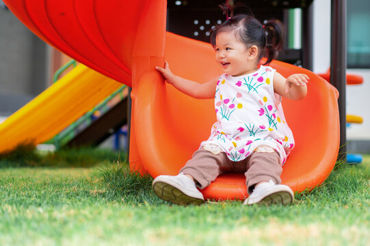 Asian cute baby playing on a slide at playground. 1 year 6 month baby enjoy and laugh at playground use as concept of play, health, mood and motion of baby and kid development.