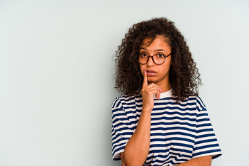 Young Brazilian woman isolated on blue background looking sideways with doubtful and skeptical expression.