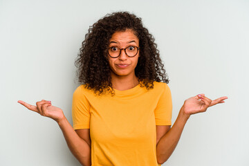 Young Brazilian woman isolated on blue background doubting and shrugging shoulders in questioning...