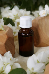 Essential oil bottle with floral scent among white jasmine flowers. Aromatherapy concept..