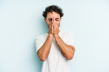 Young caucasian man isolated on blue background holding hands in pray near mouth, feels confident.