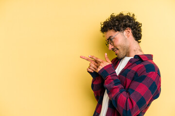 Young caucasian man isolated on yellow background points with thumb finger away, laughing and...