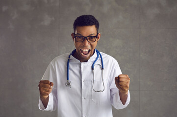 Young emotional african american doctor clenched his fists and shouted hurray. Man in glasses, a...