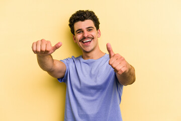 Young caucasian man isolated on yellow background raising both thumbs up, smiling and confident.