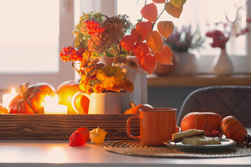 orange cup of tea and autumn decor with pumpkins, flowers and burning candles on table
