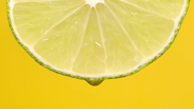 This 4k slow-motion video shows drops of water or juice dripping from a lime wedge against a yellow background, with space for a caption.