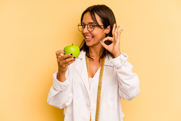 Young nutritionist woman holding a weighing machine isolated on yellow background