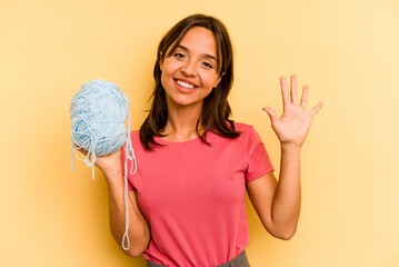 Young hispanic woman holding a ball of wool isolated on yellow background smiling cheerful showing number five with fingers.